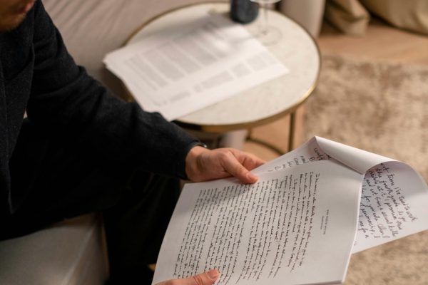 Man holding and reading documents in a cozy living room setting with wine on the side table.